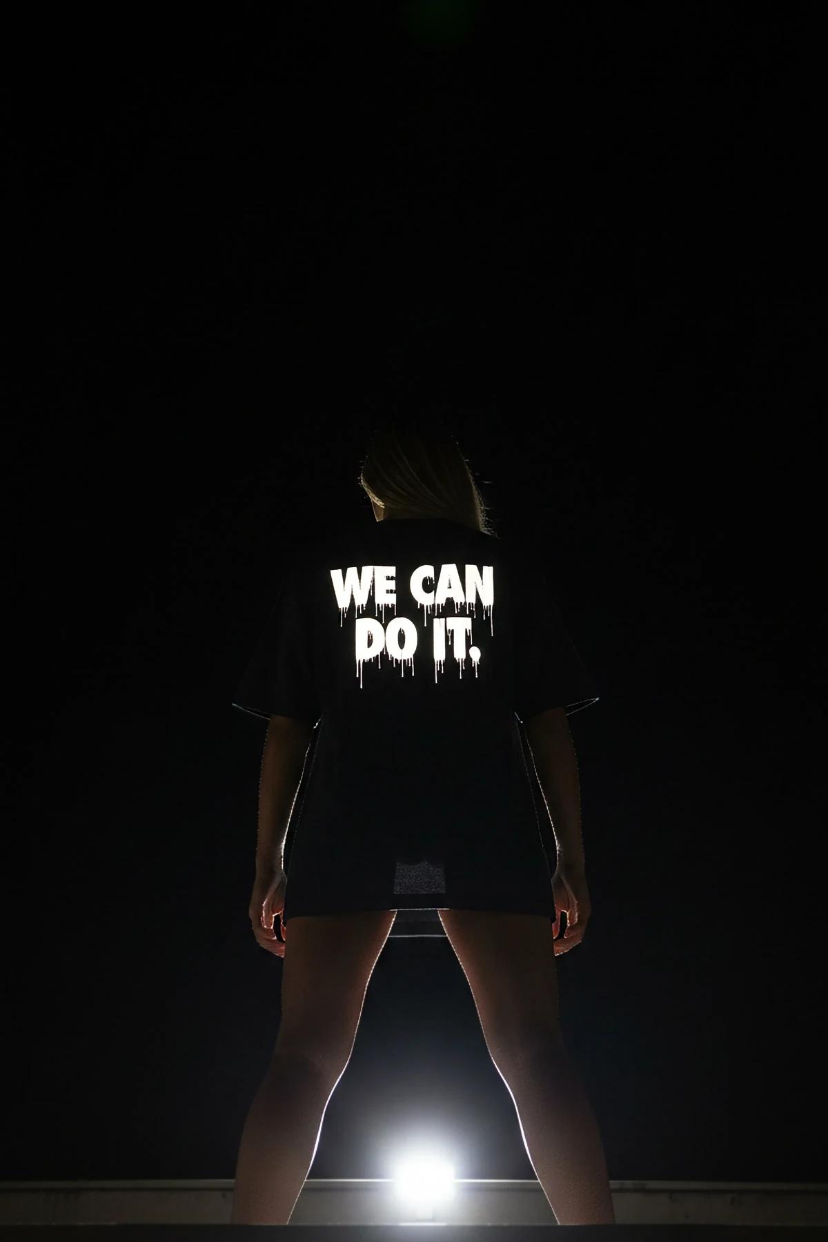 Siyah oversize tişört WE CAN DO IT reflektör baskı, gece sokak ortamında model üzerinde