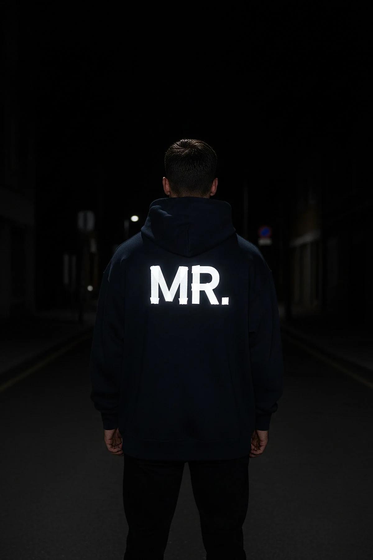Reflective navy blue hoodie with glowing MR. print on back in dark urban setting