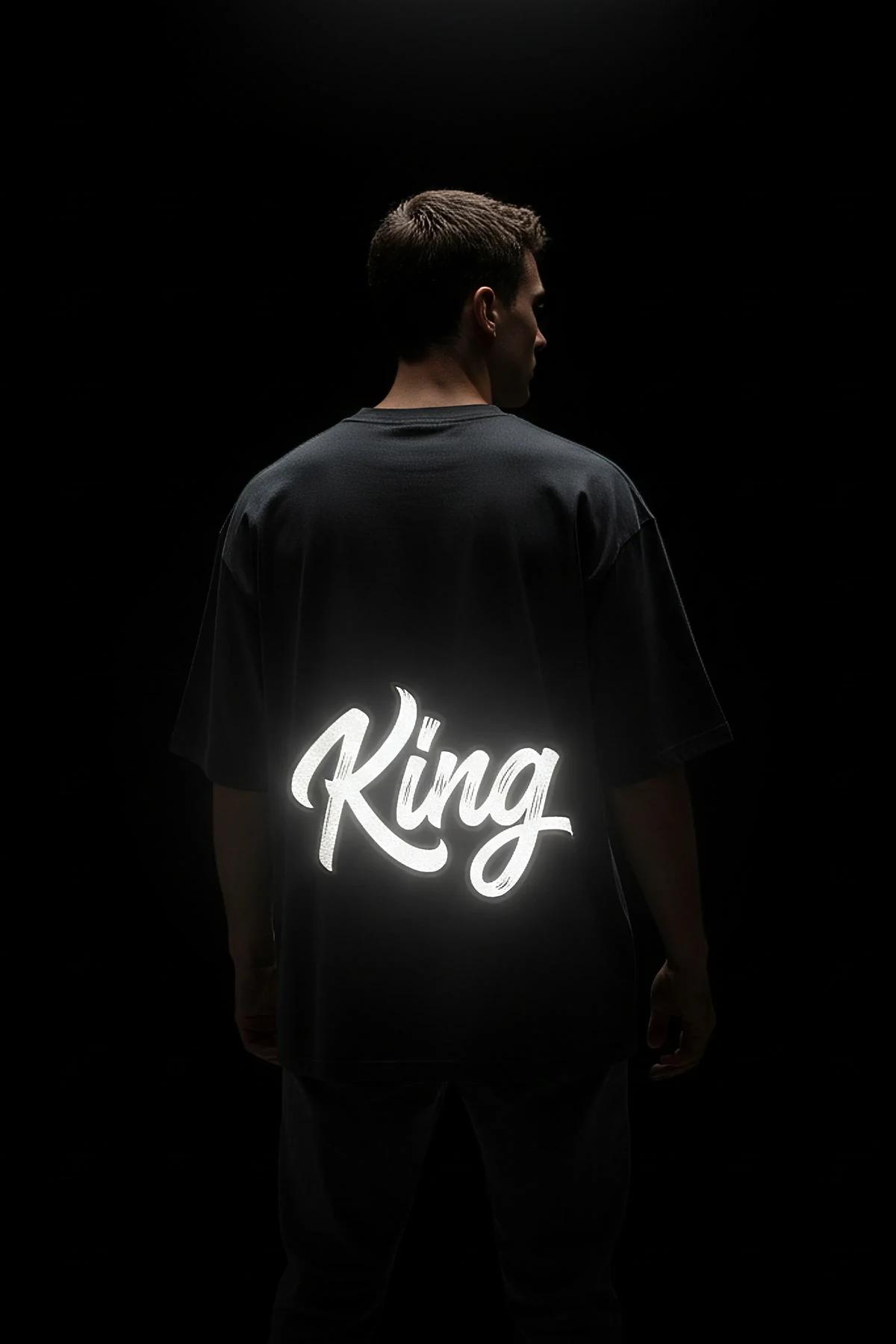 Queen ön baskılı reflektörlü siyah oversize tişört, kadın model üzerinde tam vücut görünümü karanlıkta