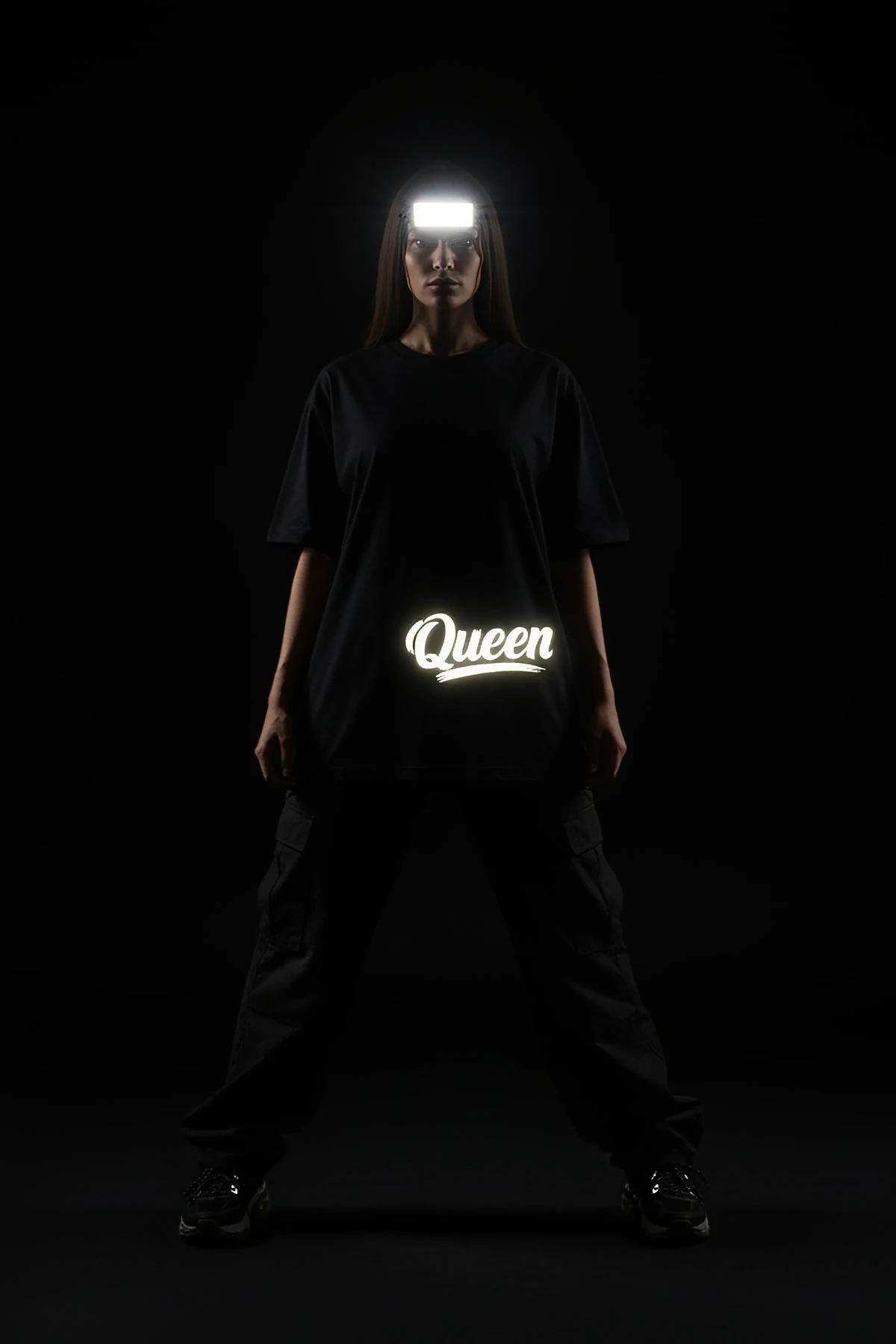 Queen ön baskılı reflektörlü siyah oversize tişört, kadın model üzerinde tam vücut görünümü karanlıkta