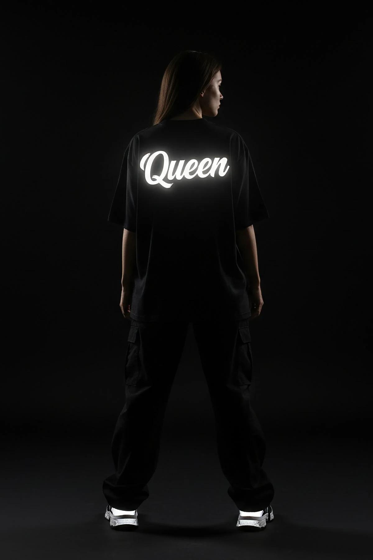 Queen ön baskılı reflektörlü siyah oversize tişört, kadın model üzerinde tam vücut görünümü karanlıkta