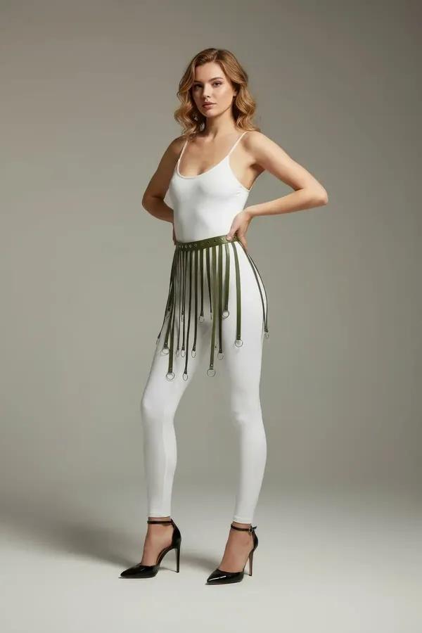 Khaki faux leather fringe skirt harness with silver O-ring tipped strands worn over white leggings