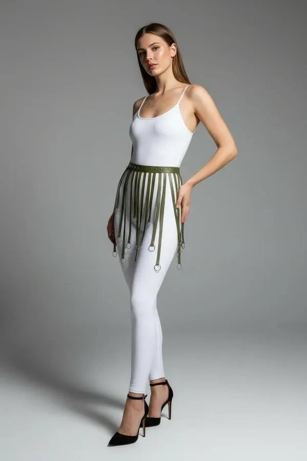 Khaki faux leather fringe skirt harness with silver O-ring tipped strands worn over white leggings
