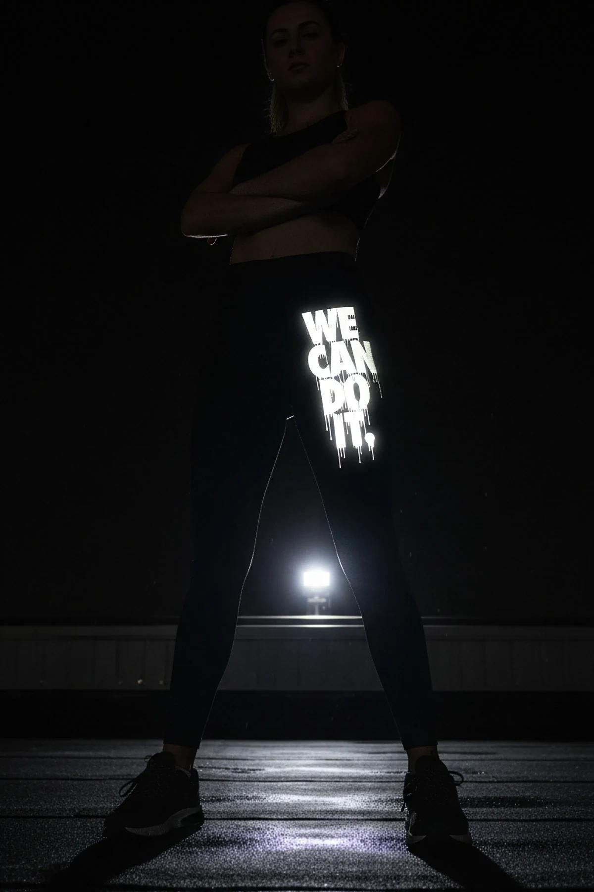 WE CAN DO IT reflektörlü sol bacak yan baskılı siyah tayt, karanlıkta ışıkla parlıyor