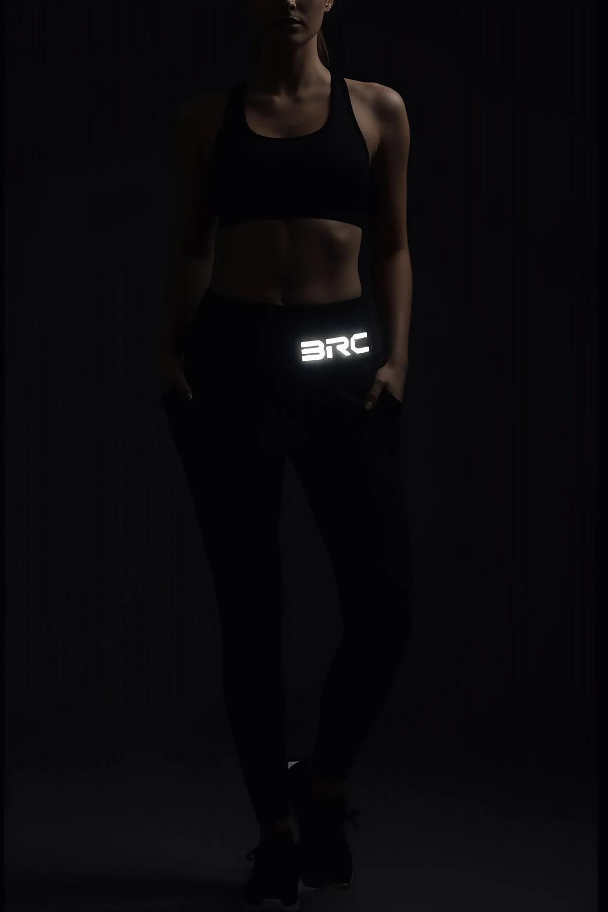 BRC reflektörlü sol bacak baskılı siyah spor tayt, ışık altında parlayan yansıtıcı yazı