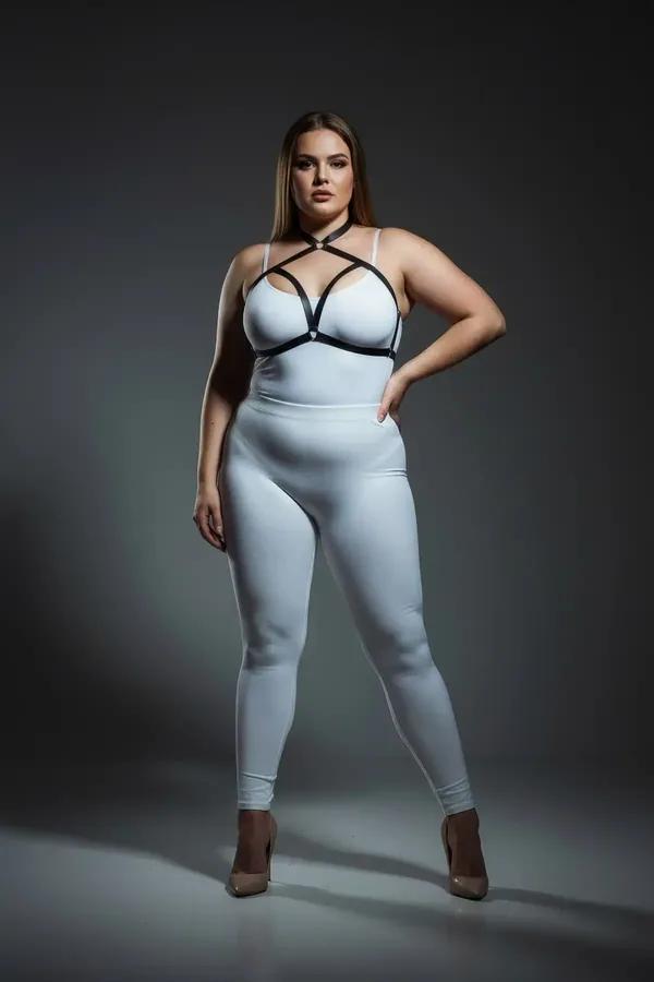 black faux leather strappy chest harness with silver O-ring geometric X-strap cage worn over white bodysuit plus size model