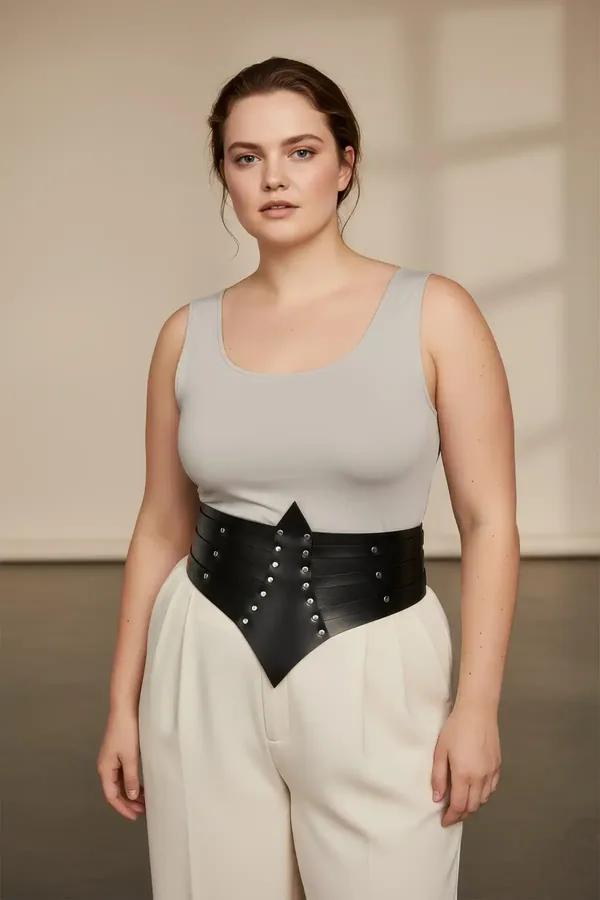 black faux leather waist cincher belt with silver dome studs and pointed chevron front panel worn over cream camisole