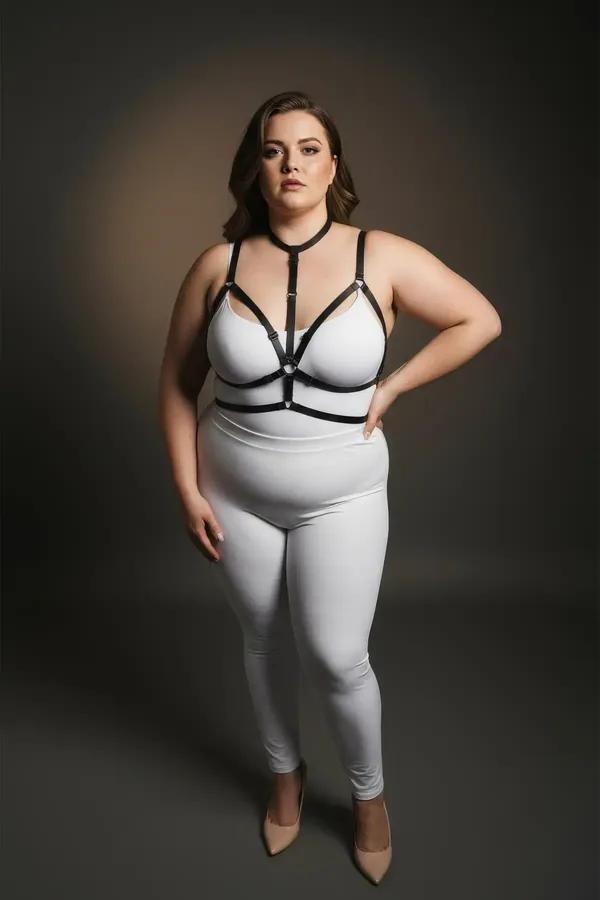 black faux leather strappy chest harness with collar neck strap and central silver O-ring worn over white bodysuit