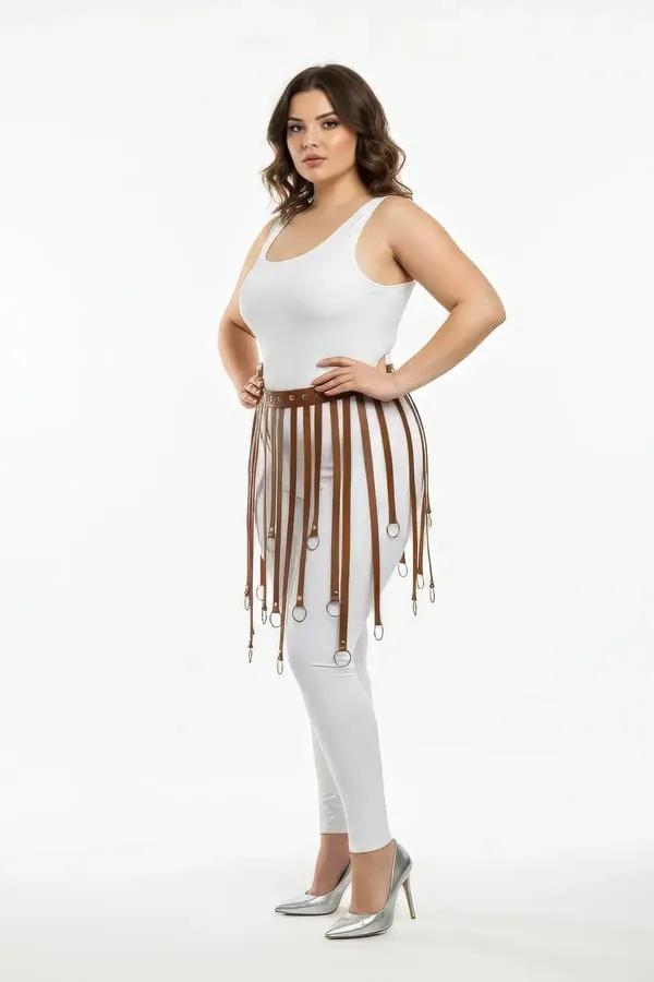 Tan faux leather fringe skirt harness with silver O-ring tipped straps worn over white leggings, plus size model