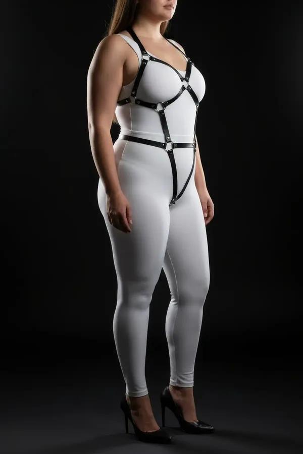 Black vegan leather full body harness with silver O-rings, wide chest frame and leg straps, worn on plus-size model