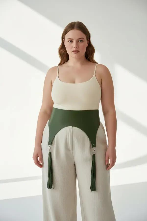 olive green wide faux leather waist harness with detachable tassels and silver clip hardware worn over white tank and beige t