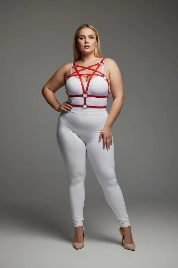 Red vegan leather starburst chest harness with silver O-rings worn over white bodysuit, plus-size model