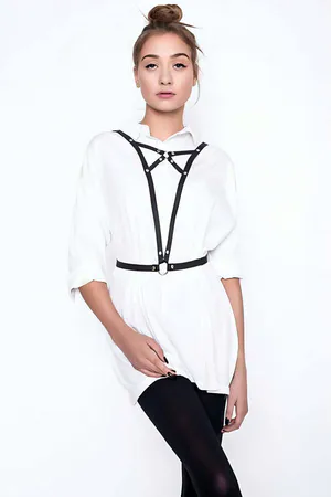 Black faux leather adjustable chest harness with central O-ring, worn over a white shirt.