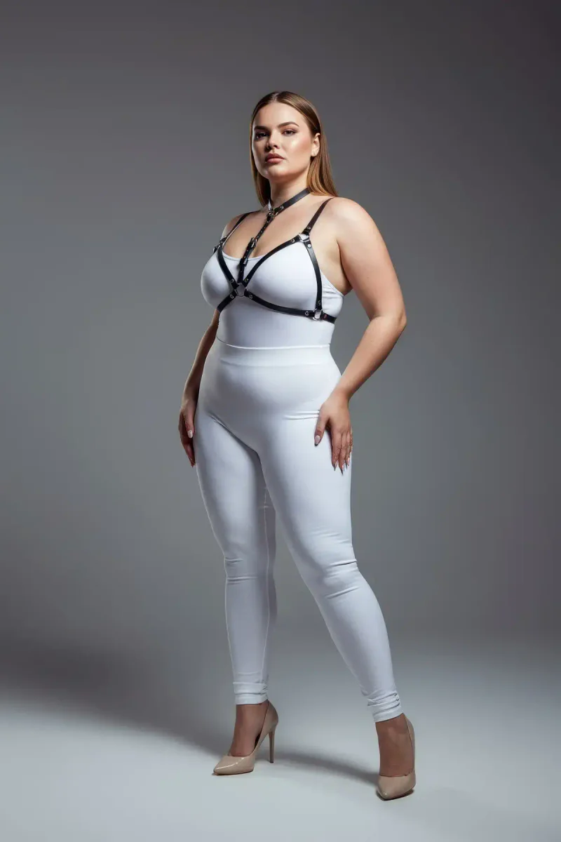 Black faux leather strappy body harness worn by a plus-size model, showing adjustable straps and O-ring detail.
